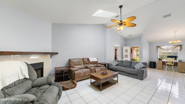 tiled living room featuring ceiling fan with notable chandelier, high vaulted ceiling, a tile fireplace, and a skylight