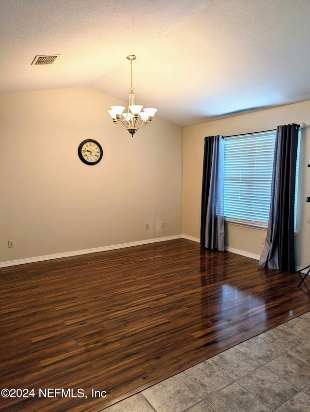 unfurnished room with vaulted ceiling, a textured ceiling, a chandelier, and dark wood-type flooring