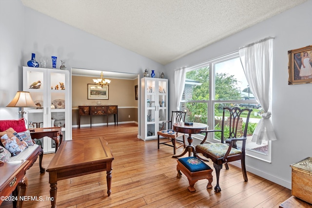 living area featuring light hardwood / wood-style floors, a textured ceiling, lofted ceiling, and a chandelier