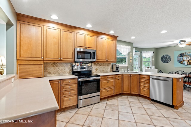 kitchen with appliances with stainless steel finishes, kitchen peninsula, sink, and light tile patterned floors