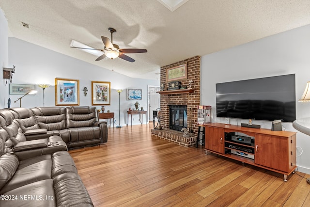 living room with lofted ceiling, ceiling fan, a textured ceiling, light wood-type flooring, and a fireplace