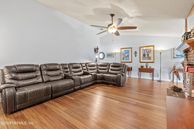 living room featuring ceiling fan, a textured ceiling, vaulted ceiling, a fireplace, and light hardwood / wood-style floors