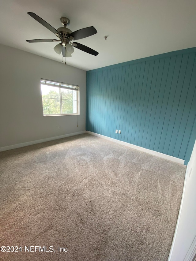 empty room featuring wood walls, carpet flooring, and ceiling fan