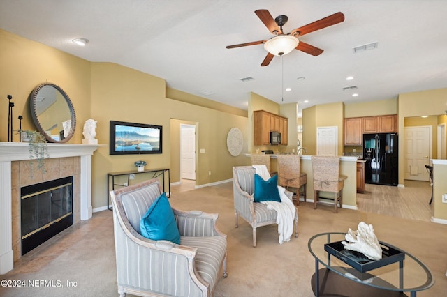 living room featuring light carpet, ceiling fan, and a tile fireplace