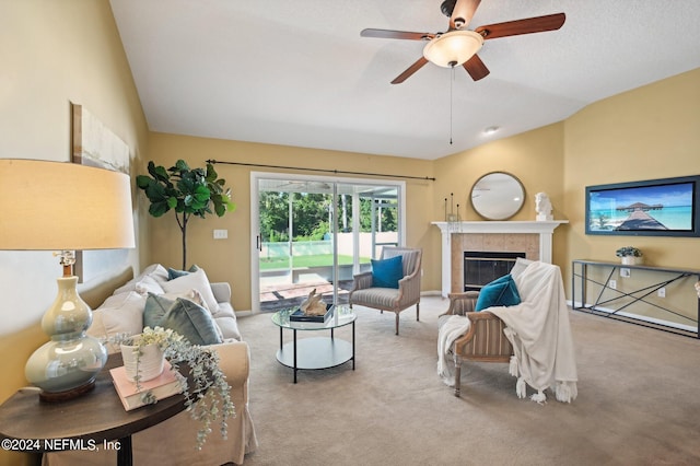 living room with ceiling fan, a tiled fireplace, vaulted ceiling, and light colored carpet