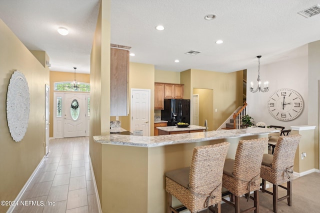 kitchen featuring hanging light fixtures, kitchen peninsula, black fridge with ice dispenser, a chandelier, and a breakfast bar