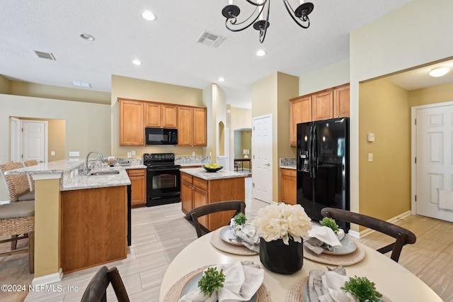 kitchen with a chandelier, sink, light stone counters, black appliances, and a center island