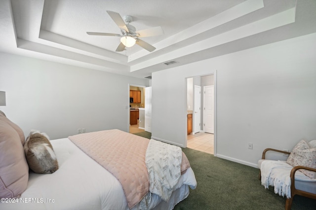 carpeted bedroom with ceiling fan, a tray ceiling, and ensuite bathroom