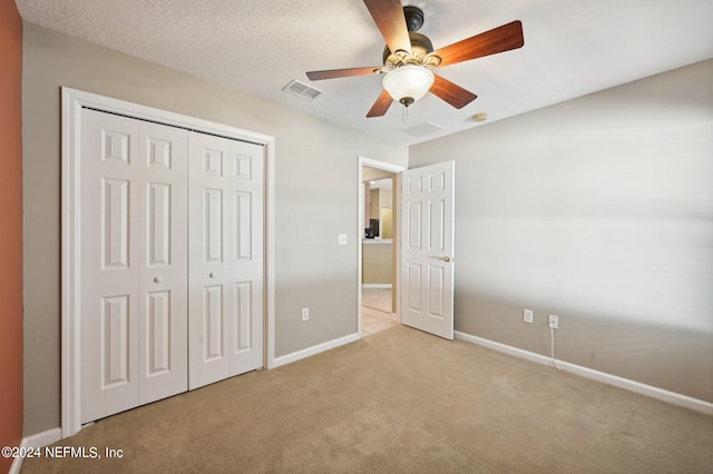 unfurnished bedroom with light carpet, ceiling fan, a closet, and a textured ceiling