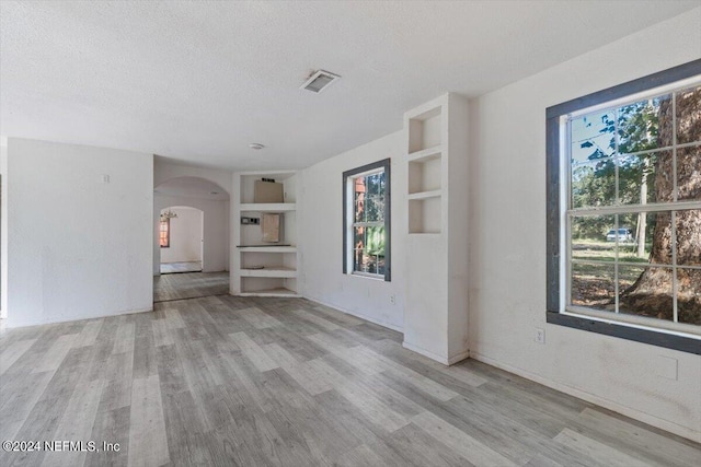 unfurnished living room featuring built in shelves, a wealth of natural light, and a textured ceiling