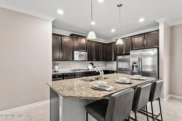 kitchen with tasteful backsplash, sink, stainless steel appliances, pendant lighting, and a kitchen island with sink