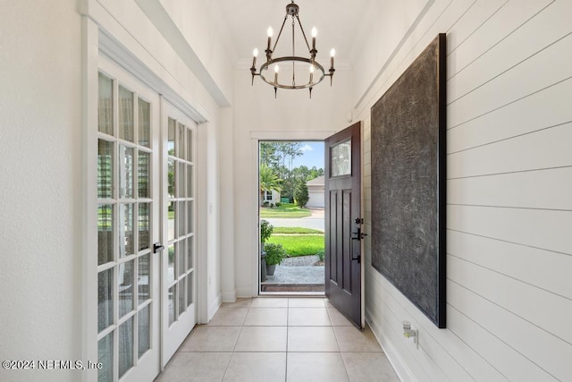 doorway with wooden walls, a chandelier, high vaulted ceiling, and light tile patterned floors