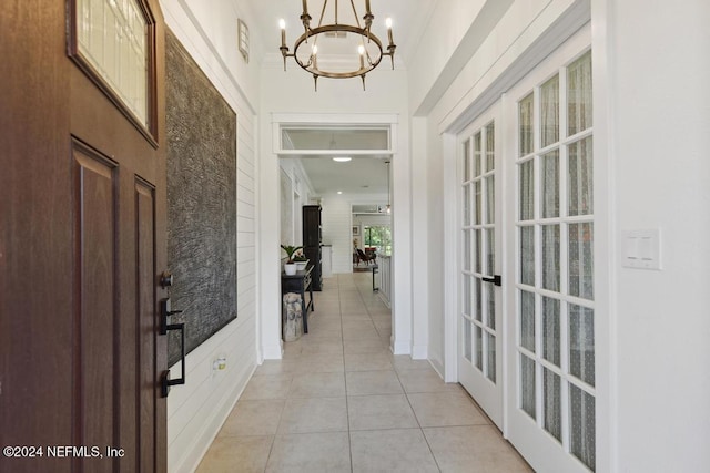 tiled foyer featuring ornamental molding, french doors, and a notable chandelier