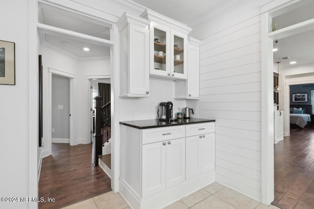 kitchen with white cabinetry, ornamental molding, dark countertops, and glass insert cabinets