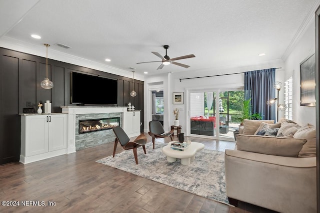 living room featuring dark wood-type flooring, a stone fireplace, crown molding, and ceiling fan