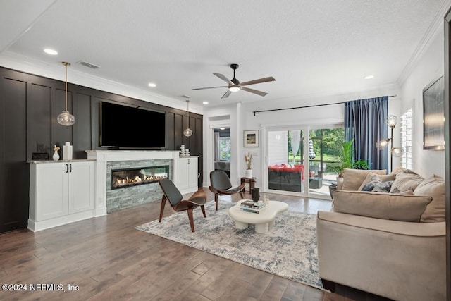 living area with crown molding, visible vents, ceiling fan, a glass covered fireplace, and dark wood-type flooring