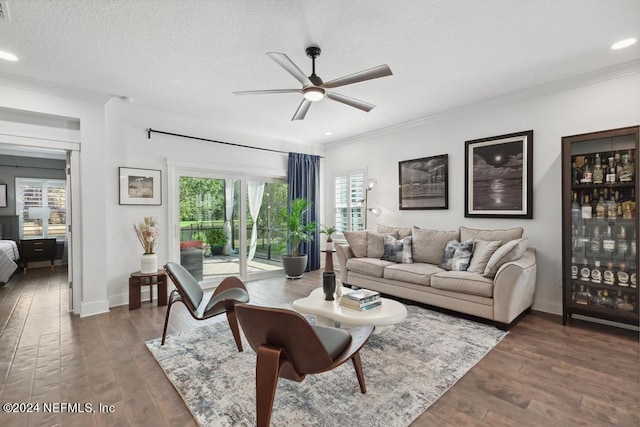 living room featuring ornamental molding, dark wood-type flooring, a textured ceiling, and ceiling fan