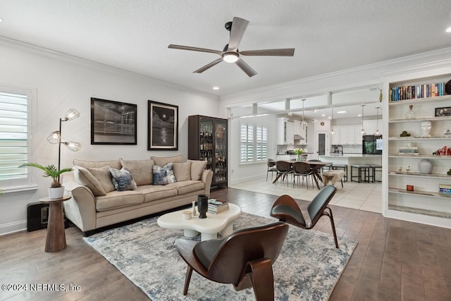 living room featuring wood-type flooring, a ceiling fan, baseboards, ornamental molding, and a textured ceiling