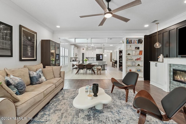 living room featuring crown molding, visible vents, a glass covered fireplace, light wood-type flooring, and a ceiling fan