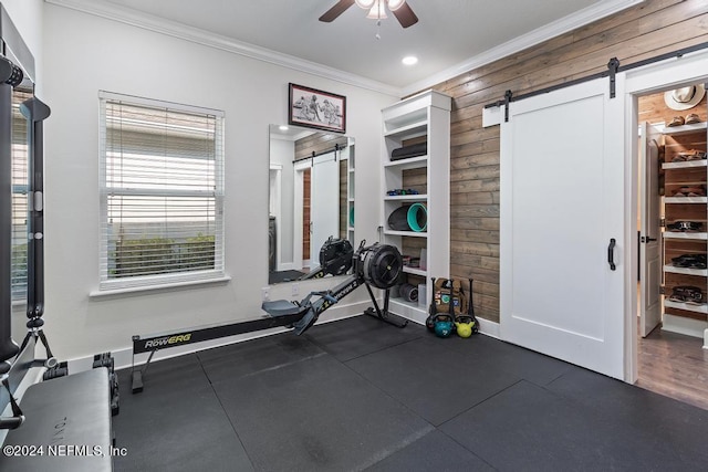 workout room with a barn door, baseboards, wooden walls, ornamental molding, and a ceiling fan