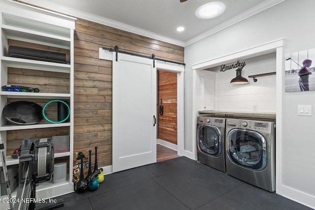 laundry area featuring washer and dryer, a barn door, ornamental molding, wood walls, and dark tile patterned flooring