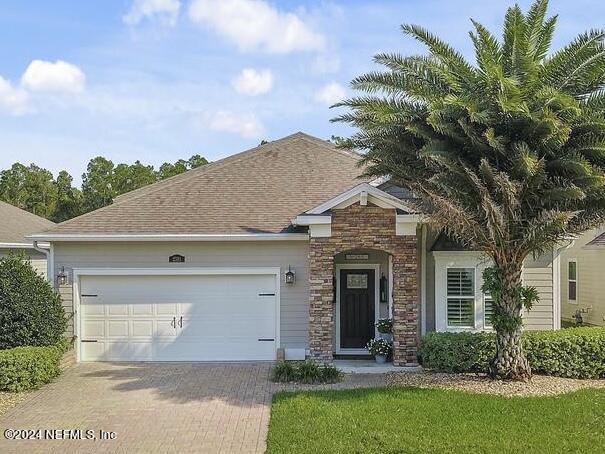 view of front of house with stone siding, decorative driveway, roof with shingles, and a garage