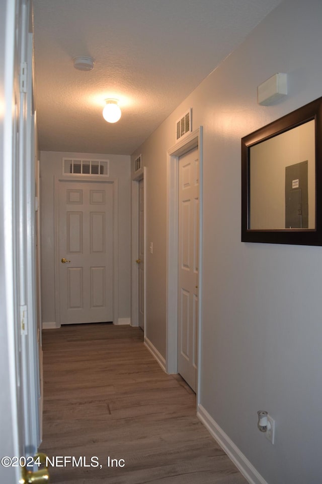 hallway with a textured ceiling and wood-type flooring