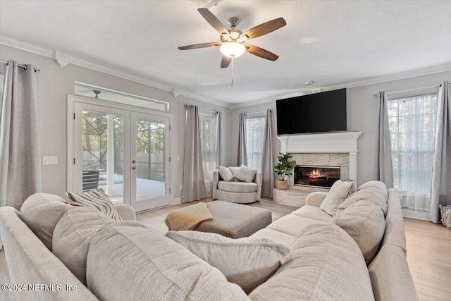 living room featuring a tiled fireplace, a wealth of natural light, light wood-type flooring, and french doors