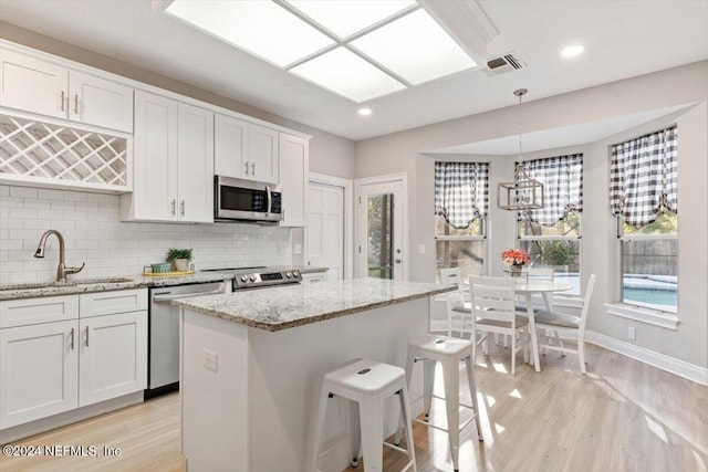 kitchen featuring sink, white cabinetry, hanging light fixtures, a kitchen island, and stainless steel appliances