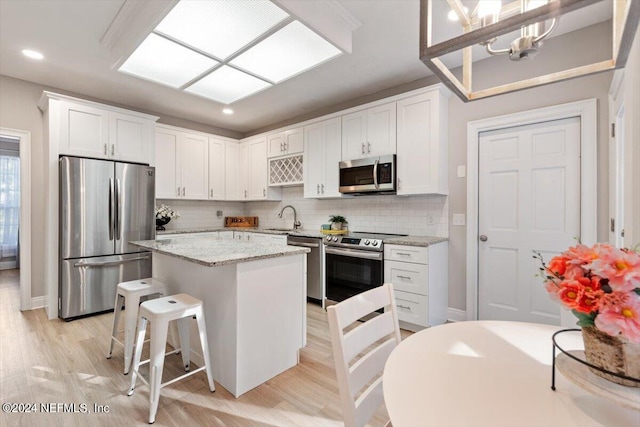 kitchen with a kitchen island, appliances with stainless steel finishes, sink, white cabinets, and light stone counters