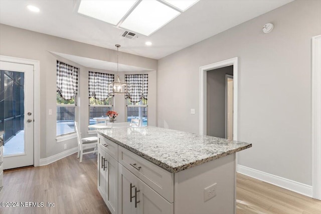 kitchen with light stone counters, a kitchen island, light hardwood / wood-style floors, and hanging light fixtures