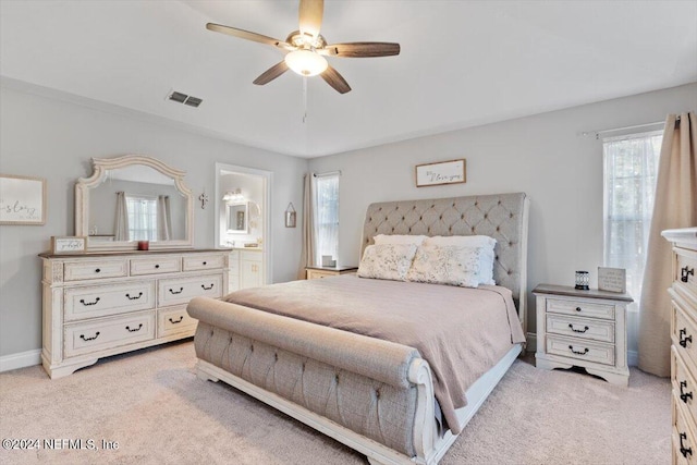 bedroom featuring ceiling fan, light colored carpet, and ensuite bath