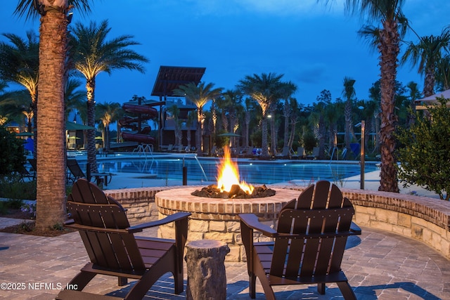 pool at dusk with a patio, pool water feature, and a fire pit