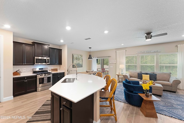 kitchen with pendant lighting, sink, stainless steel appliances, and light hardwood / wood-style floors