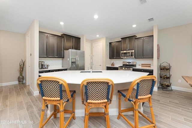 kitchen with appliances with stainless steel finishes, dark brown cabinets, light hardwood / wood-style floors, and an island with sink