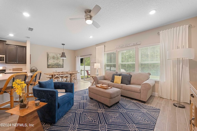 living room with a textured ceiling, light hardwood / wood-style floors, and ceiling fan