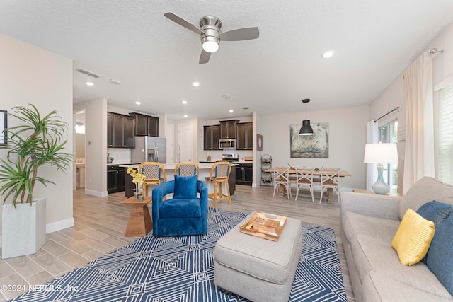 living room with light hardwood / wood-style flooring, a textured ceiling, and ceiling fan