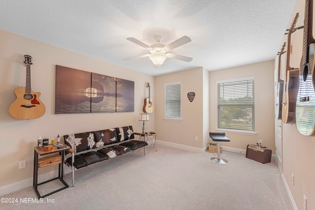 living area with ceiling fan, a textured ceiling, and light colored carpet