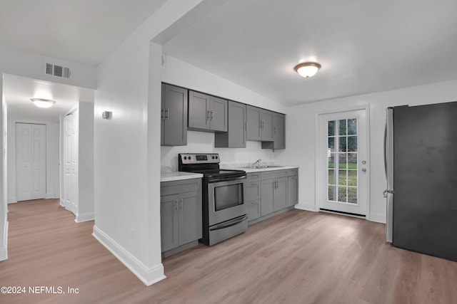 kitchen with appliances with stainless steel finishes, sink, gray cabinets, light hardwood / wood-style floors, and lofted ceiling