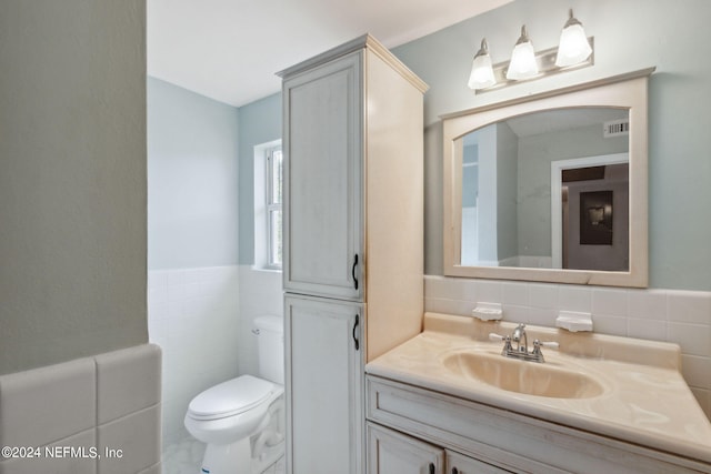 bathroom with vanity, toilet, and tile walls