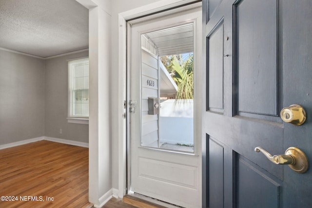 doorway with ornamental molding, a textured ceiling, and wood-type flooring