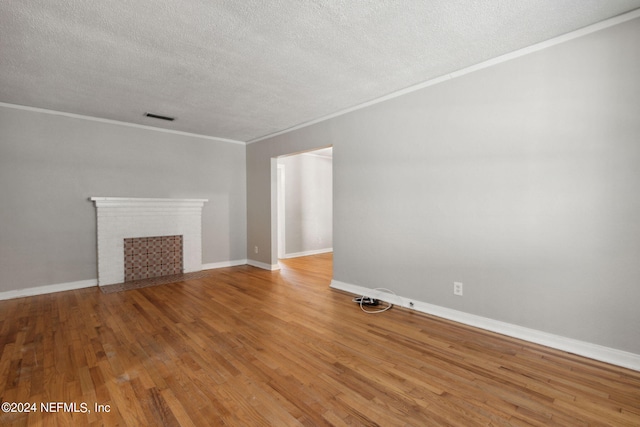 unfurnished living room with crown molding, a textured ceiling, wood-type flooring, and a brick fireplace