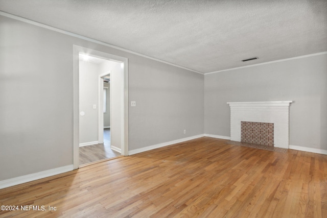 unfurnished living room with crown molding, wood-type flooring, a textured ceiling, and a brick fireplace