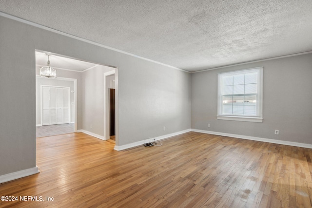 unfurnished room with wood-type flooring, a textured ceiling, a chandelier, and ornamental molding