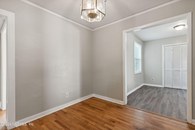 empty room featuring hardwood / wood-style floors, crown molding, and an inviting chandelier