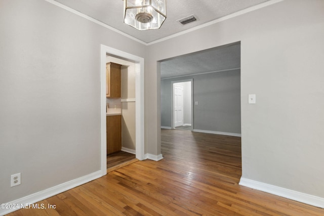 interior space with a textured ceiling, wood-type flooring, ornamental molding, and a chandelier