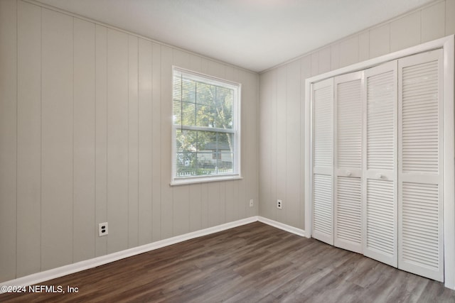 unfurnished bedroom featuring a closet, wood walls, and hardwood / wood-style floors