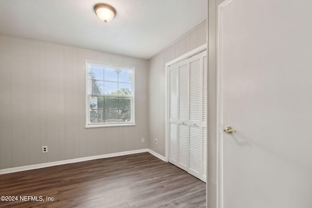 unfurnished bedroom featuring a closet, dark hardwood / wood-style floors, and wood walls