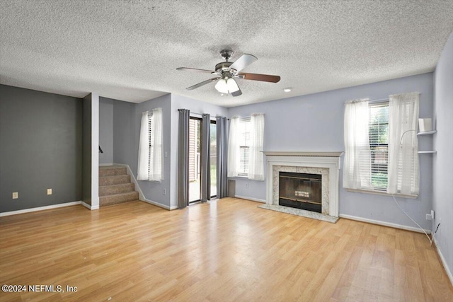 unfurnished living room featuring a premium fireplace, light hardwood / wood-style flooring, a textured ceiling, and ceiling fan