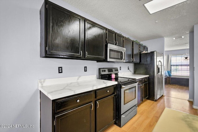 kitchen with appliances with stainless steel finishes, light hardwood / wood-style flooring, a textured ceiling, and light stone countertops